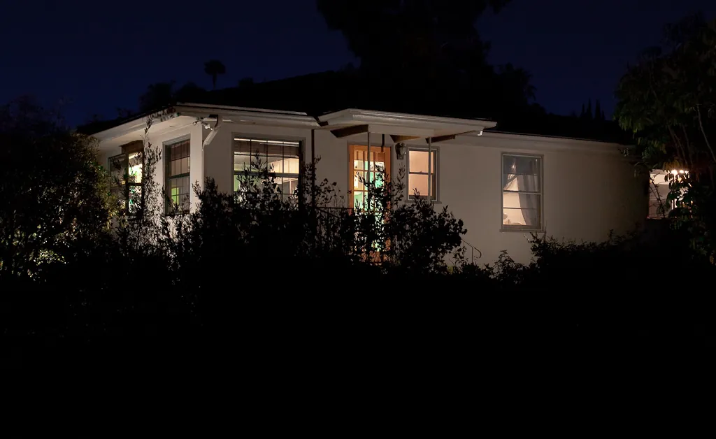 Front of a home at night with lit windows and shrubs