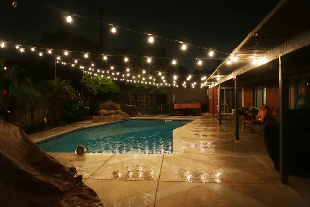 Patio string lights reflecting on a pool deck at night