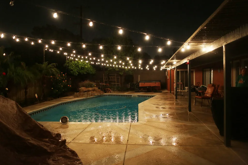 Patio string lights reflecting on a pool deck at night