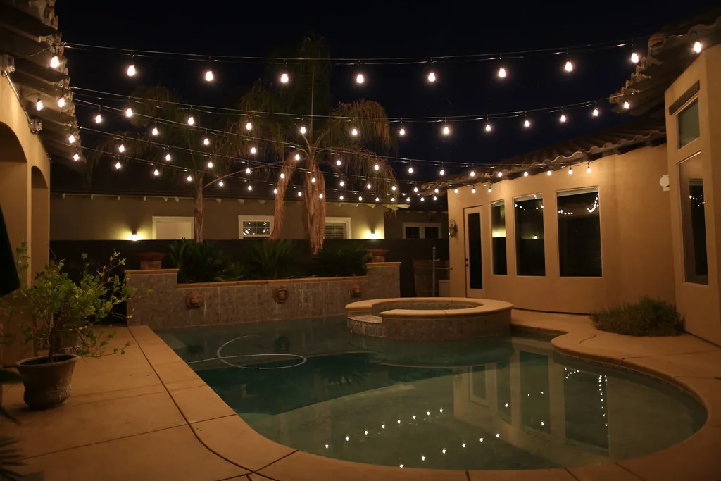 Lit pool courtyard with string lights and accent lighting at night
