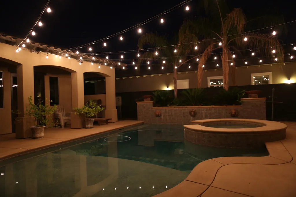 Courtyard pool, spa and stucco home lit at night with string lights