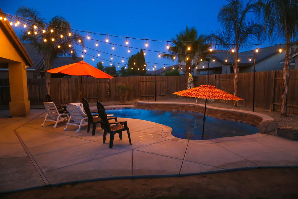 Pool deck with bistro string lights, umbrellas and palms at blue hour