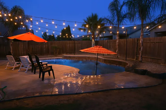 Backyard pool and patio at dusk under warm string lights and palm trees